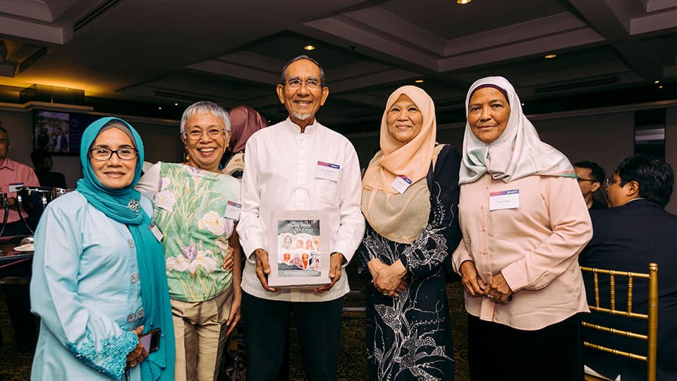 Four alumni at the Vice-Chancellor's reception in Malaysia. They are standing together and smiling and one is holding a book.