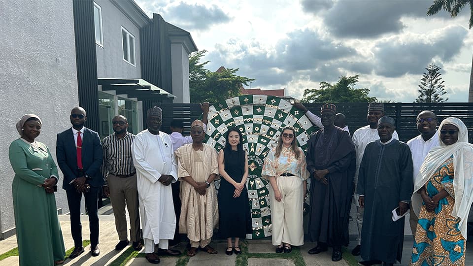 The Alumni Engagement Team and alumni in Abuja standing together with a special handmade tapestry.