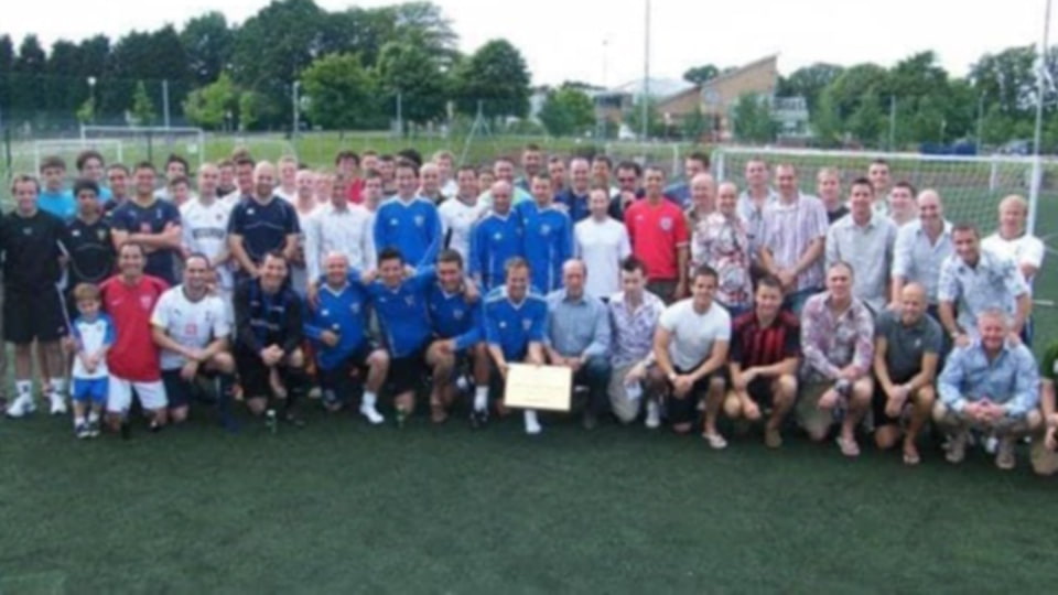 A group of football alumni standing and squatting together on a field