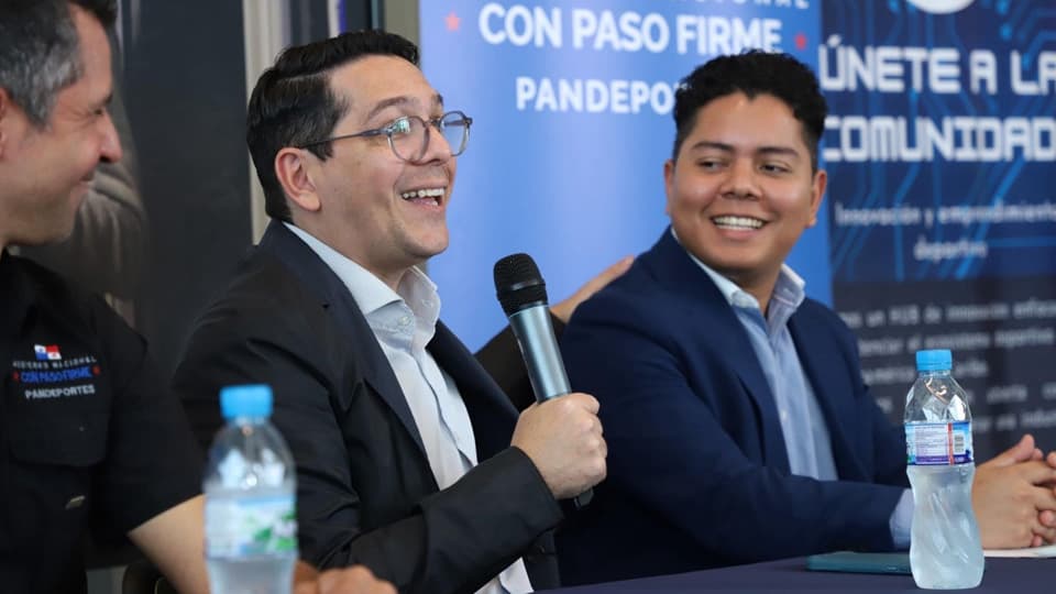 Two people seated on a panel discussion stage, with one holding a microphone while speaking.