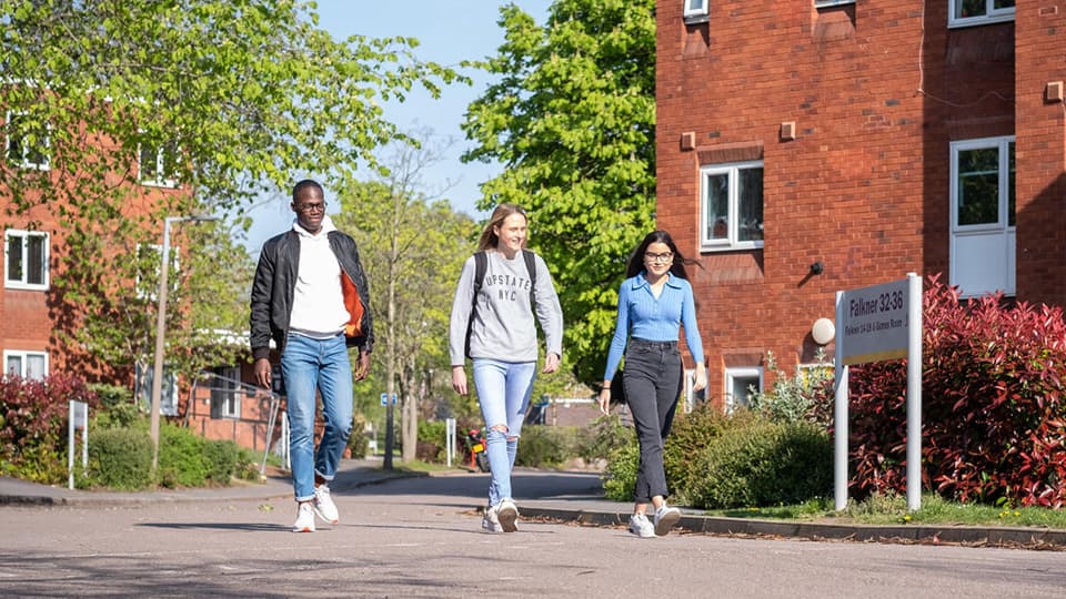 three students walking through the green space in front of the Falkner Eggington accommodation on Loughborough University campus