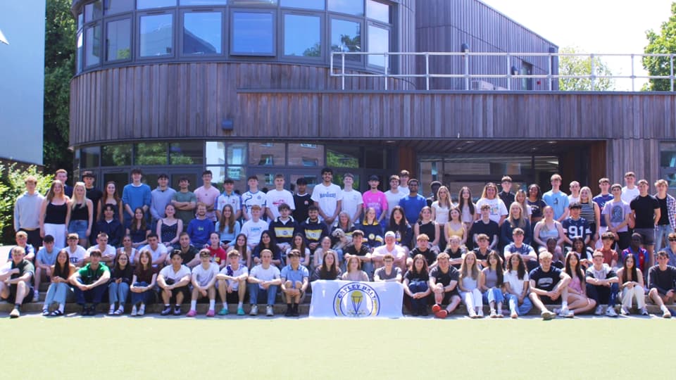 A large group of students gathered for a group photo outside a wooden building.