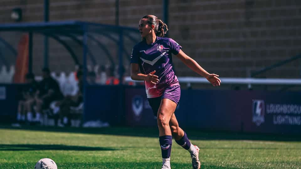 A lightning player is dribbling the ball at her feet on the football pitch.