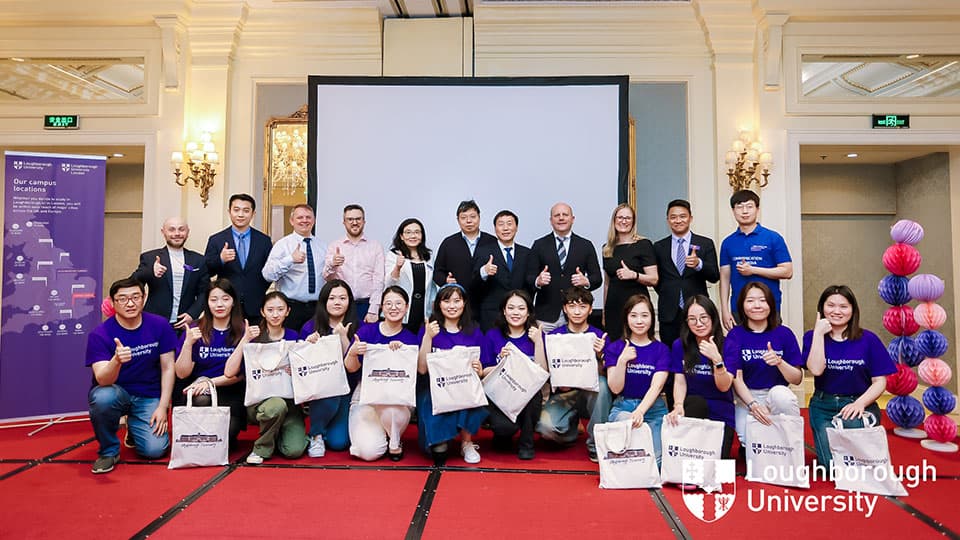 A group shot of alumni wearing Loughborough University t-shirts and prospective students along with other attendees standing and smiling at the camera at Loughborough University's Beijing alumni event.