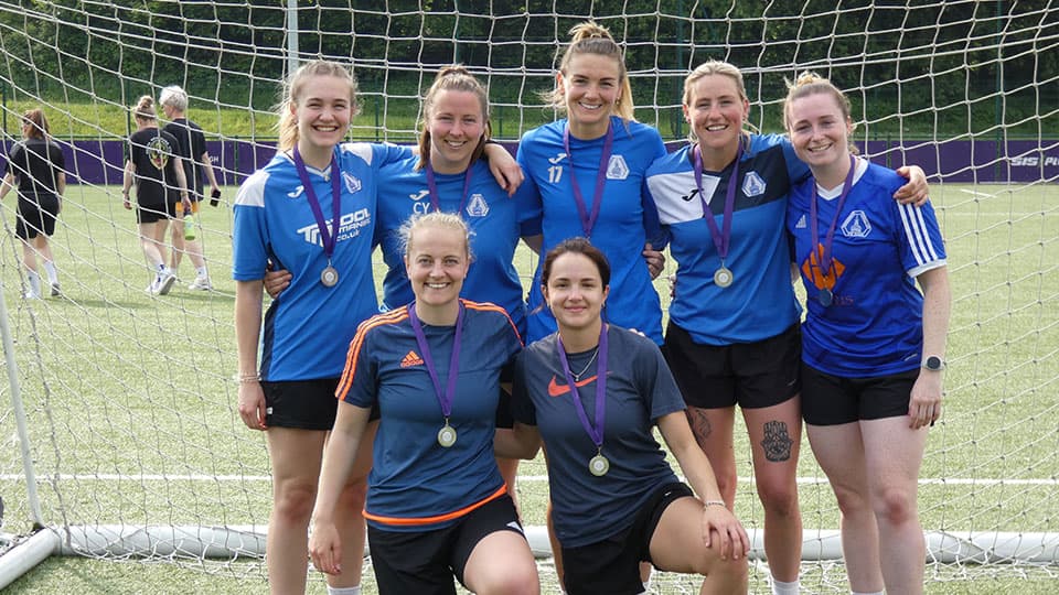 A group of women wearing blue football shirts in front of a goal at Hollywell Sports Complex, Loughborough University