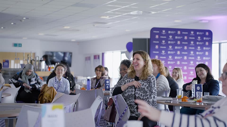 A shot of the women who attended Loughborough University's Women's in Enterprise Conference. They are smiling and focusing on who is speaking at the front of the room.
