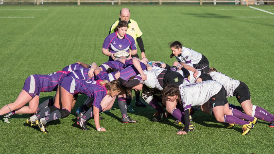 Female rugby players engaging in a rugby scrum on a pitch.