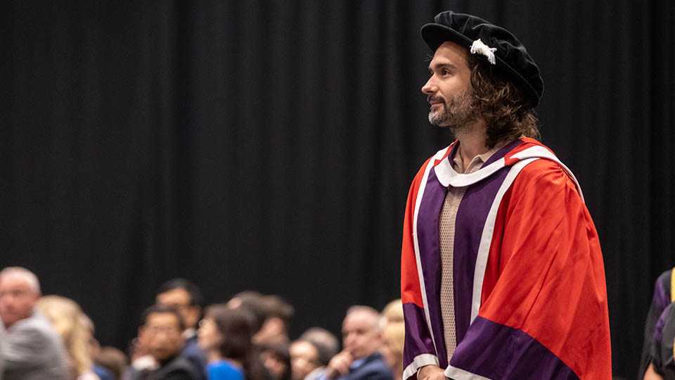 Joe Wicks stood on the stage looking out, wearing a graduation gown and hat