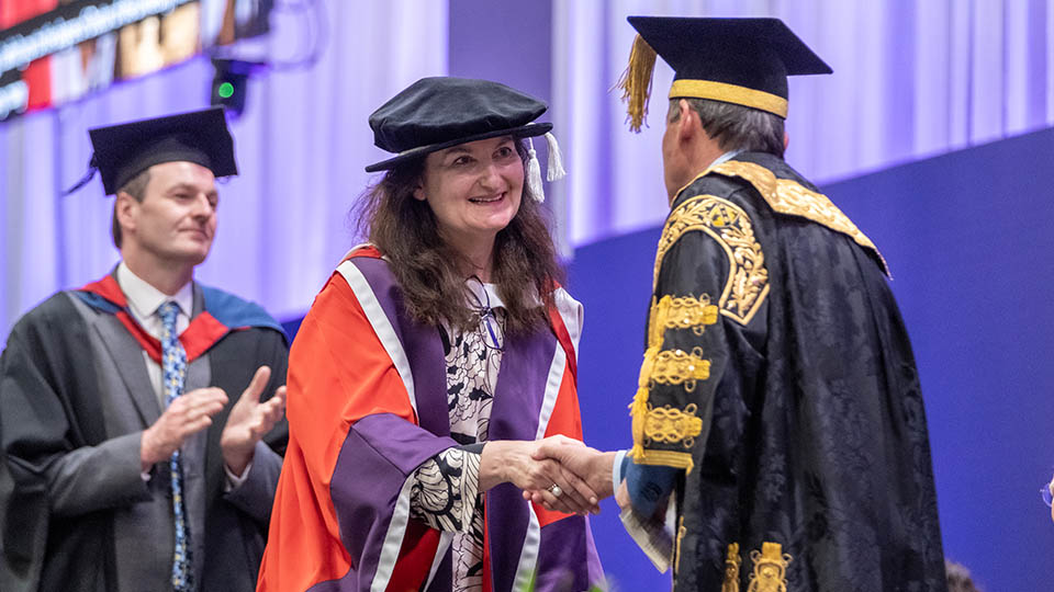 Miriam smiling and shaking hands with Chancellor Lord Seb Coe on the graduation stage