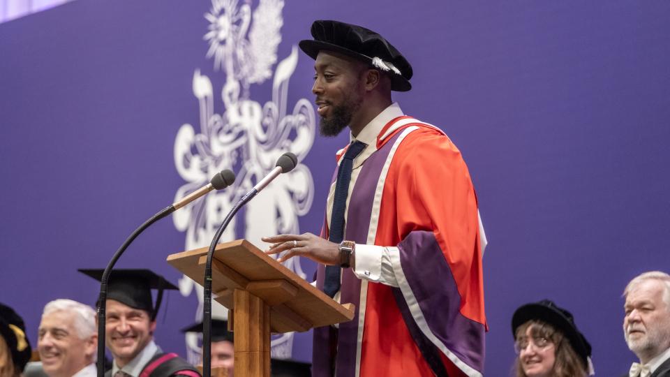 Nana Badu stood at a lecturn speaking to the audience at a graduation ceremony