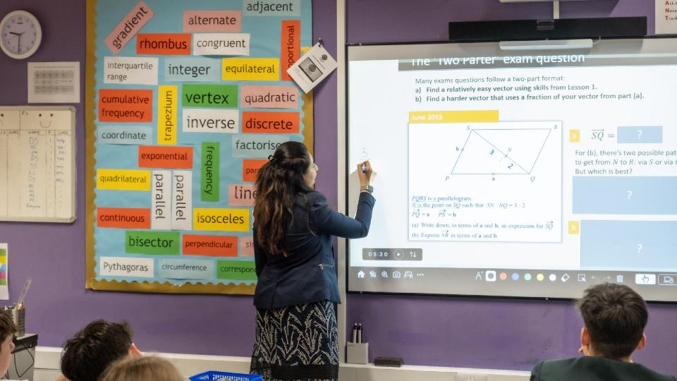 Student teacher stood in a classroom by a whiteboard teaching students about maths