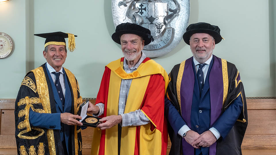 Professor Smith stood smiling with his University Medal, next to Lord Seb Coe and Vice-Chancellor Prof Nick Jennings