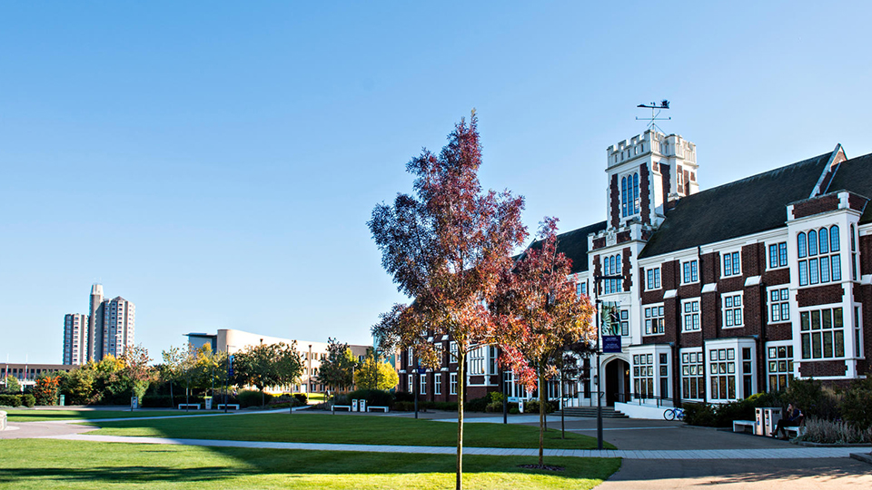 Side view of the outside of Hazlerigg Building with the lawn and an autumnal tree in front