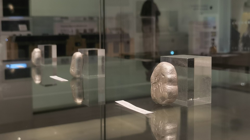 Three silver pebble-sized brooches of abstract shape engraved with simple animal drawings inside a glass display case.