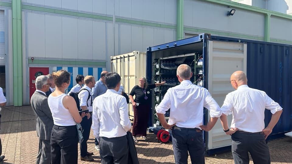 Delegates visiting one of the battery electrolyser container systems intended for storage of electricity and generation of hydrogen, that is being built on campus.