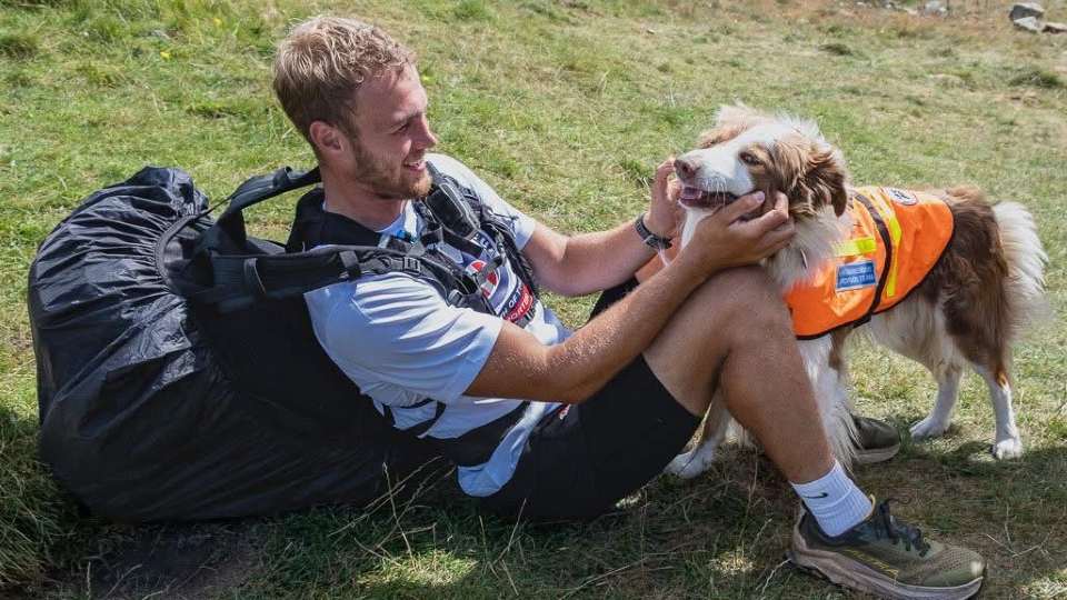 Hal Hodkinson sitting on the ground petting a dog wearing a mountain rescue team vest.