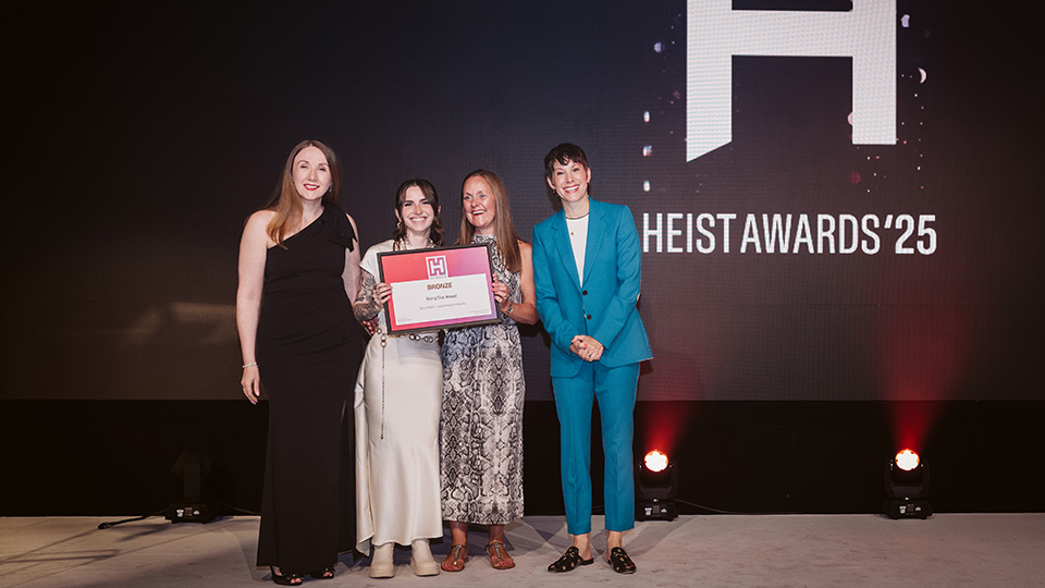 Four people standing on stage holding a certificate at the HEIST Awards ceremony.