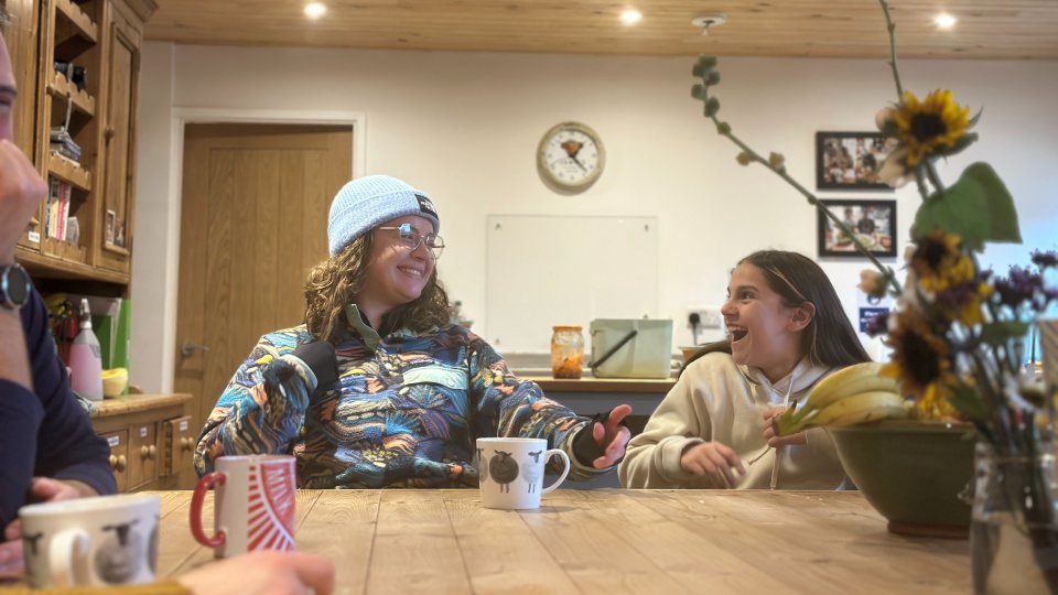 A photo of a teenage girl sitting next to a young woman, looking at each other with joyful expressions.