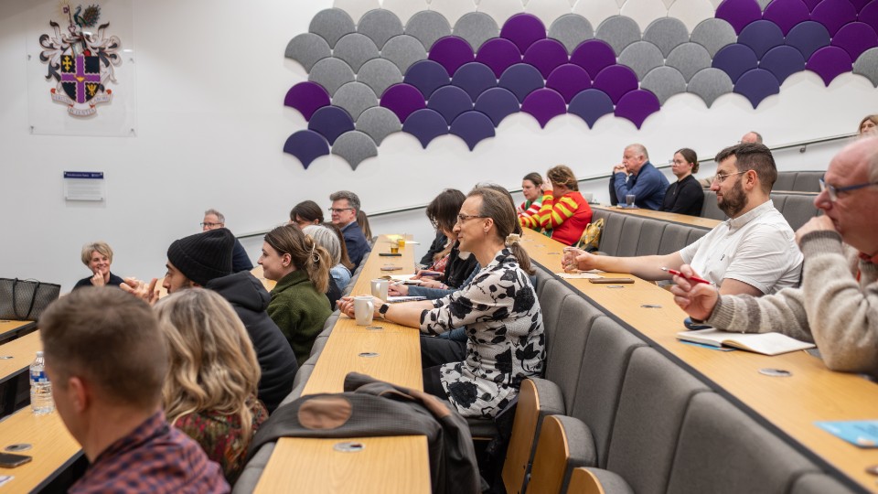 A group of people sat in a lecture theatre talking and smiling.
