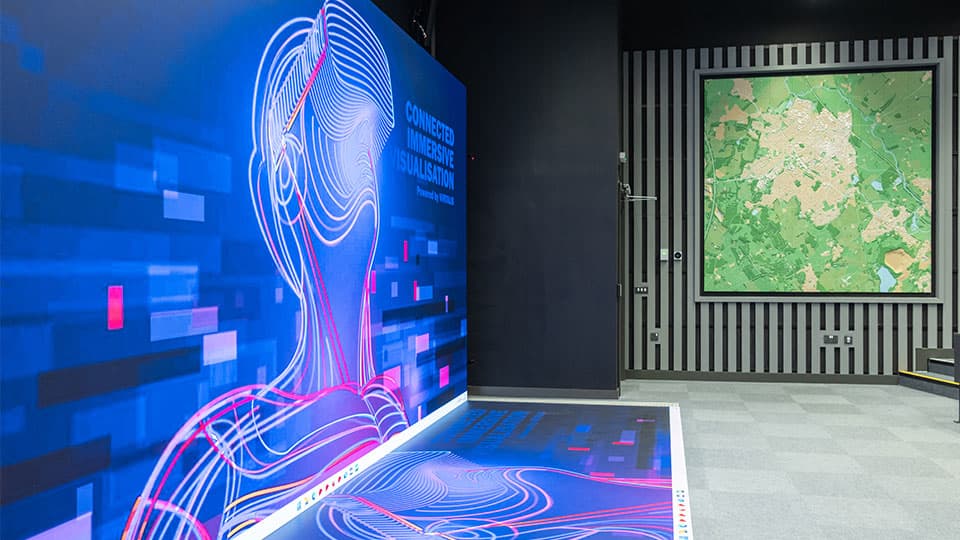 A wall to floor screen in Digilab Central showing a brightly-coloured futuristic person wearing a Virtual Reality headset while looking upwards