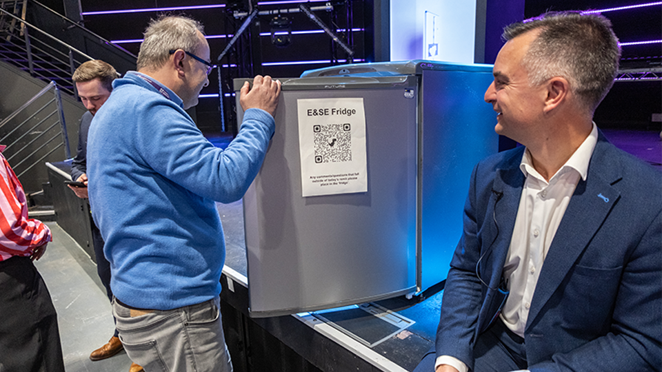 Professor Sam Grogan sat down watching a member of staff put a written idea into a fridge on the stage