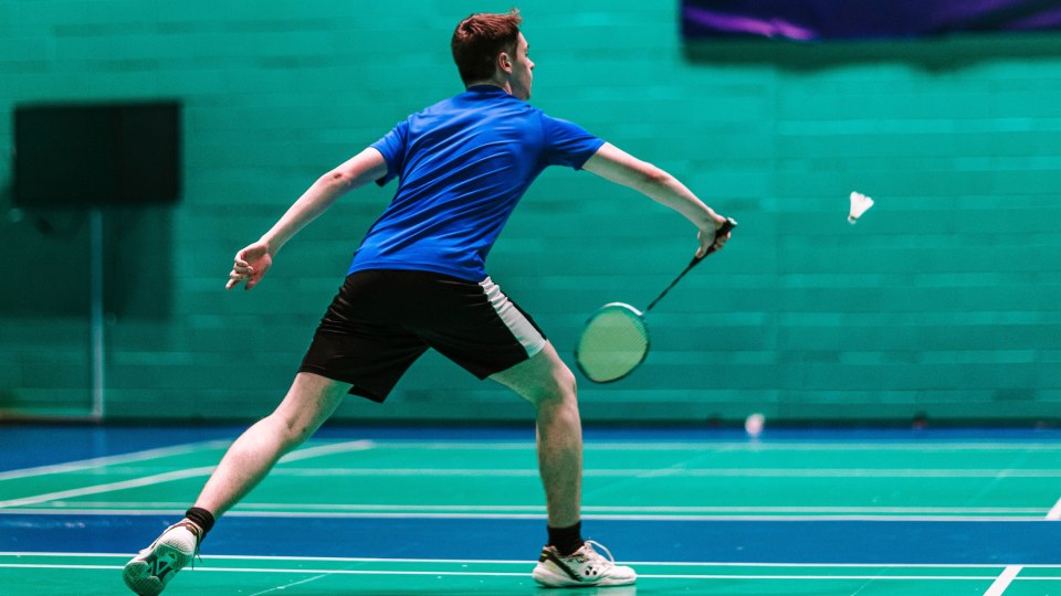 A student lunging to hit a shuttlecock with a badminton racket.