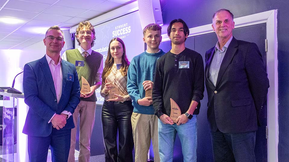 Four students holding trophies posing with two members of staff.