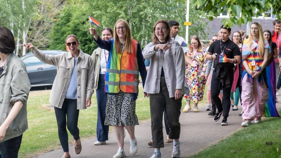 Staff and students smiling and waving rainbow flags whilst walking outside