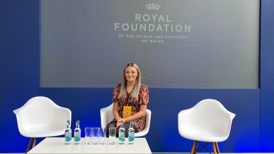One student sitting between two empty chairs, the Royal Foundation logo is on the wall behind.