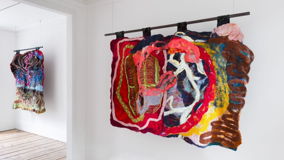 Colourful tapestries made of felt hanging in a gallery.