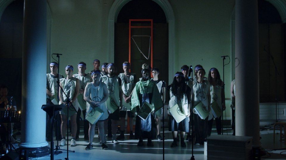 A choir standing together in a dark room behind microphone stands.